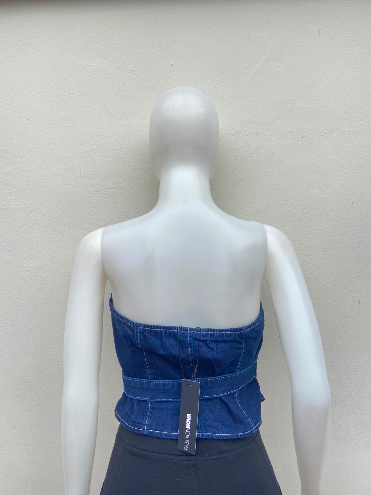 Top jean azul, con zíper al frente y detalle de lazo ajustable.