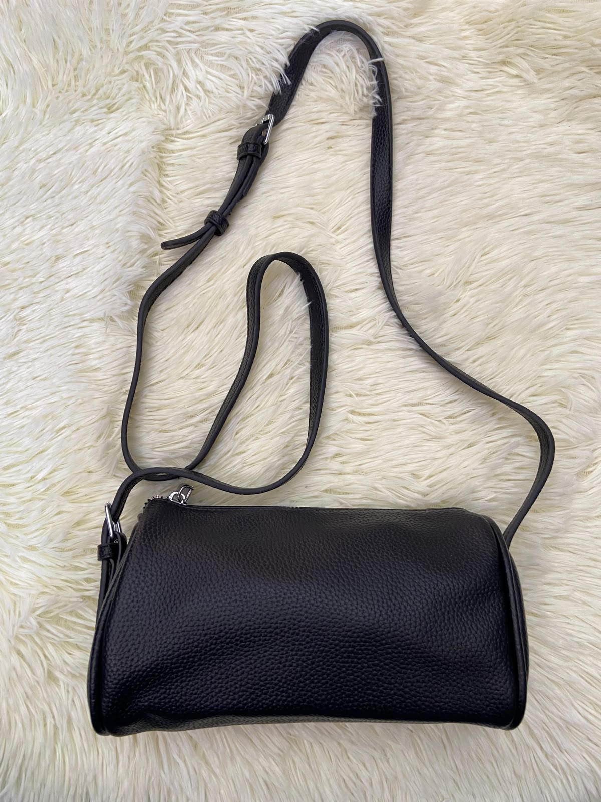 Cartera, negra pequeña con lazo ajustable, en forma de cilindro.