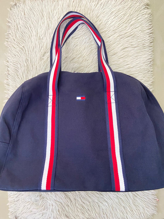 Bulto Tommy Hilfiger Original en color azul marino con logotipo de la marca al frente y lazos en color azul marino rojo y blanco.
