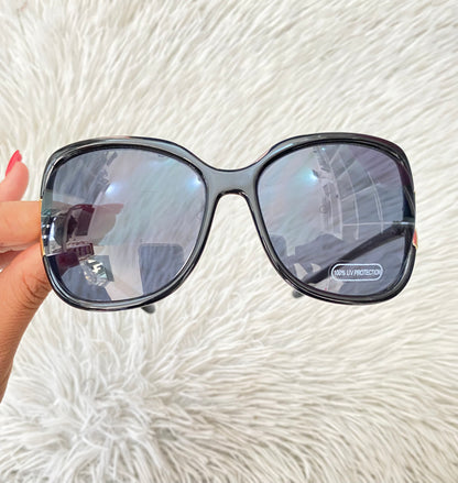 Lentes negro, ovalados, con detalle dorado en la esquina y micas claras PROTECCIÓN UV 100