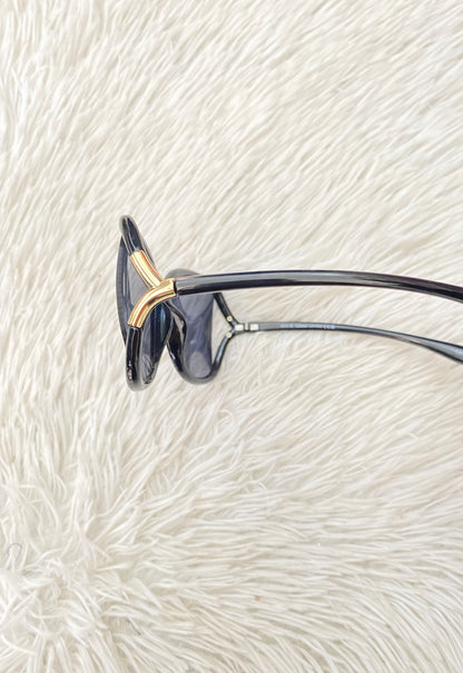 Lentes negro, ovalados, con detalle dorado en la esquina y micas claras PROTECCIÓN UV 100