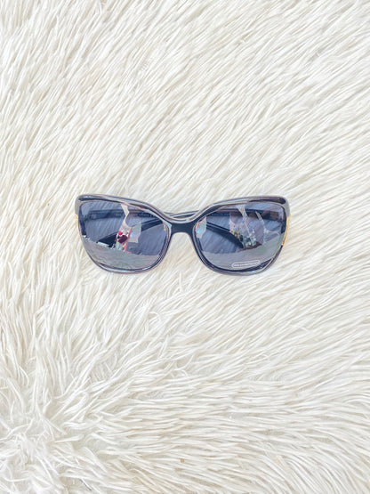Lentes negro, ovalados, con detalle dorado en la esquina y micas claras PROTECCIÓN UV 100