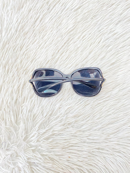 Lentes negro, ovalados, con detalle dorado en la esquina y micas claras PROTECCIÓN UV 100