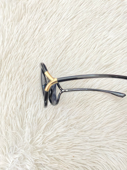 Lentes negro, ovalados, con detalle dorado en la esquina y micas claras PROTECCIÓN UV 100