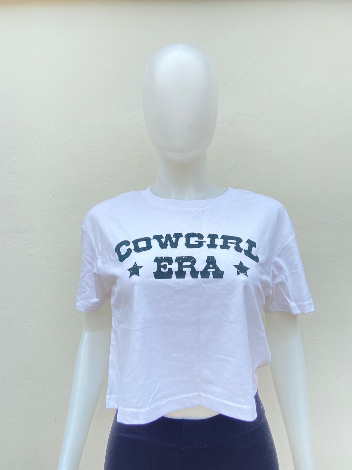 Top blanco, con letras negras “COWGIRL ERA” ( Etapa Vaquera).