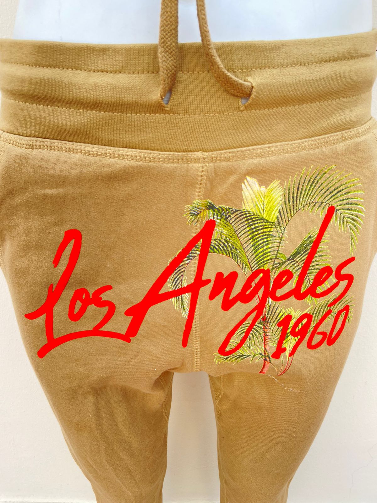 Pantalon/ Jogger FASHION NOVA original, color caqui con letras LOS ÁNGELES 1960 en color naranja en el centro y palmeras verdes.