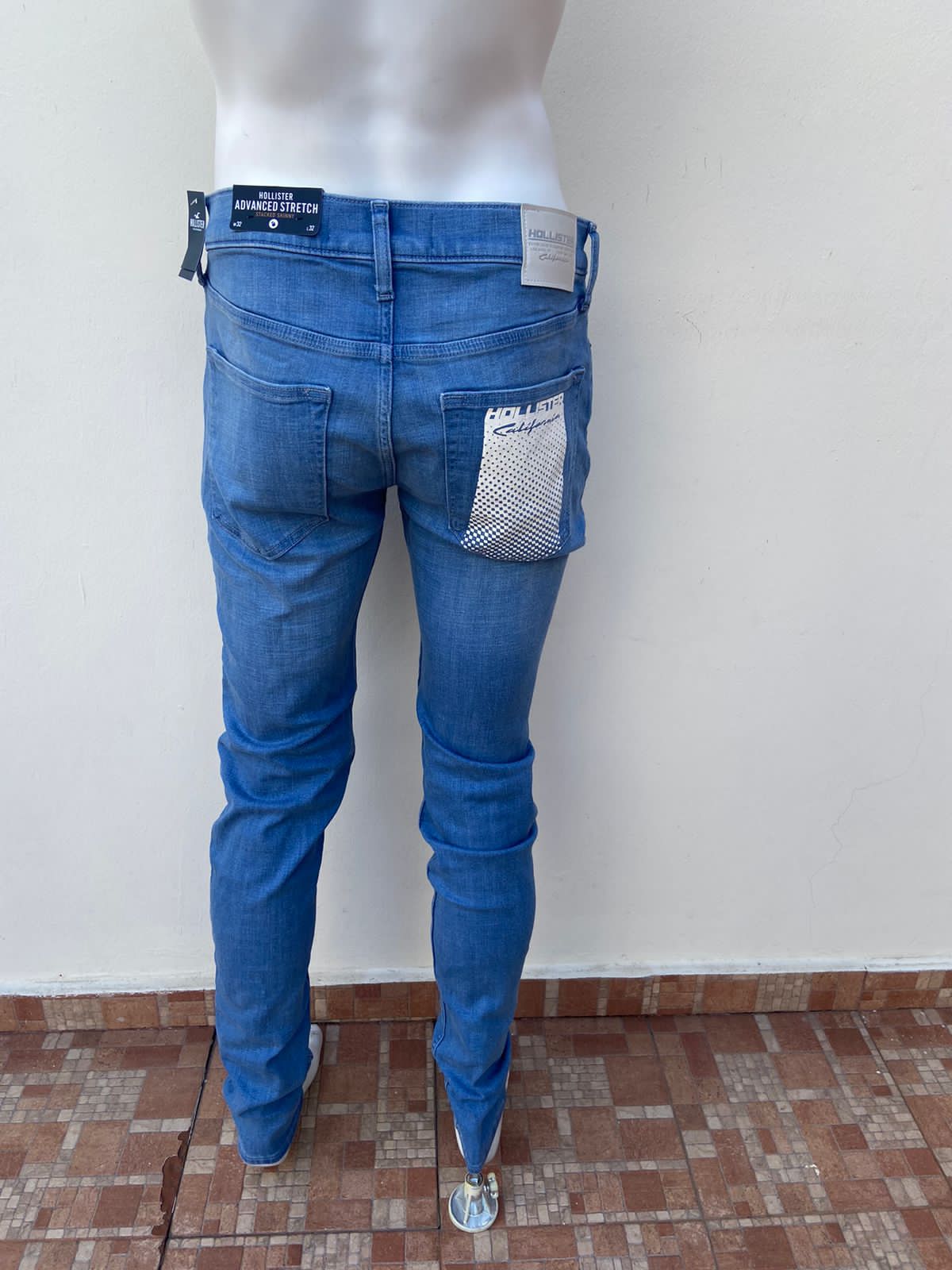 Pantalon jeans Hollister original azul claro con rasgados al frente y diseño de letra HOLLISTER CALIFORNIA en la parte de atrás con recuadro blanco ADVANCE STRETCH STACKED SKINNY