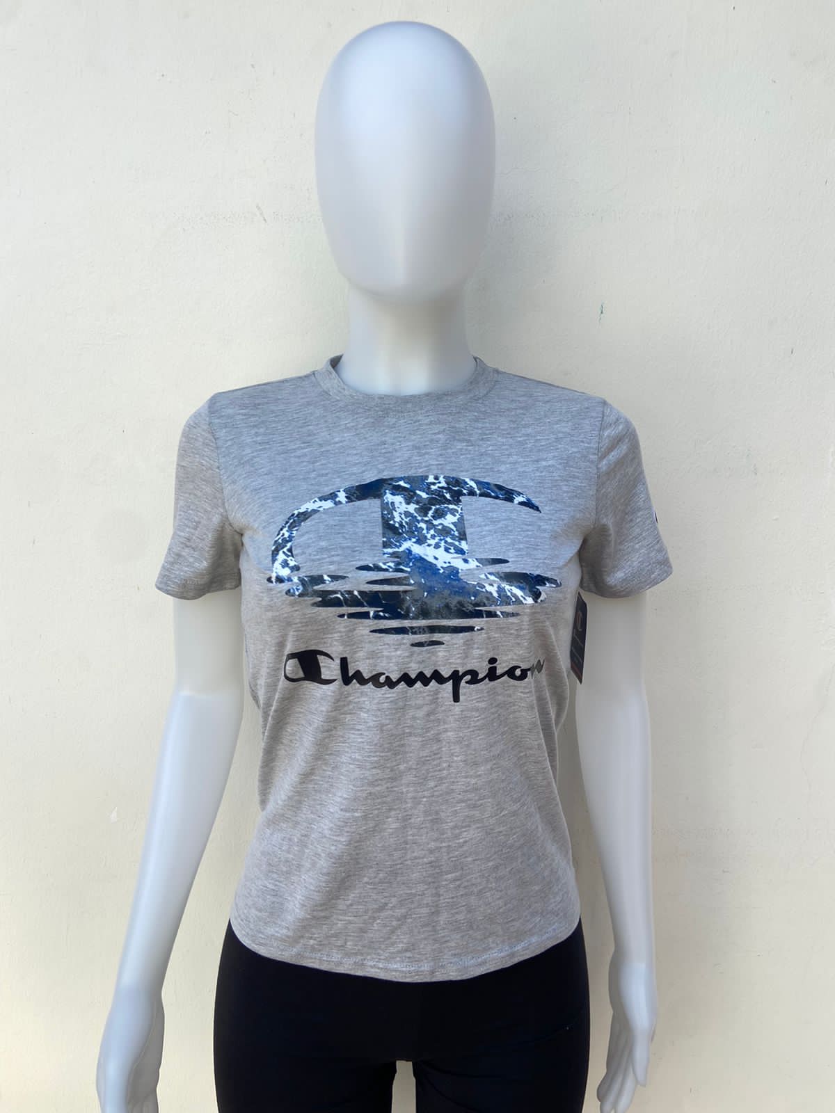 T-shirt Champion original, gris con logotipo de la marca en color azul, gris y blanco y letras CHAMPION en color negro en el centro.