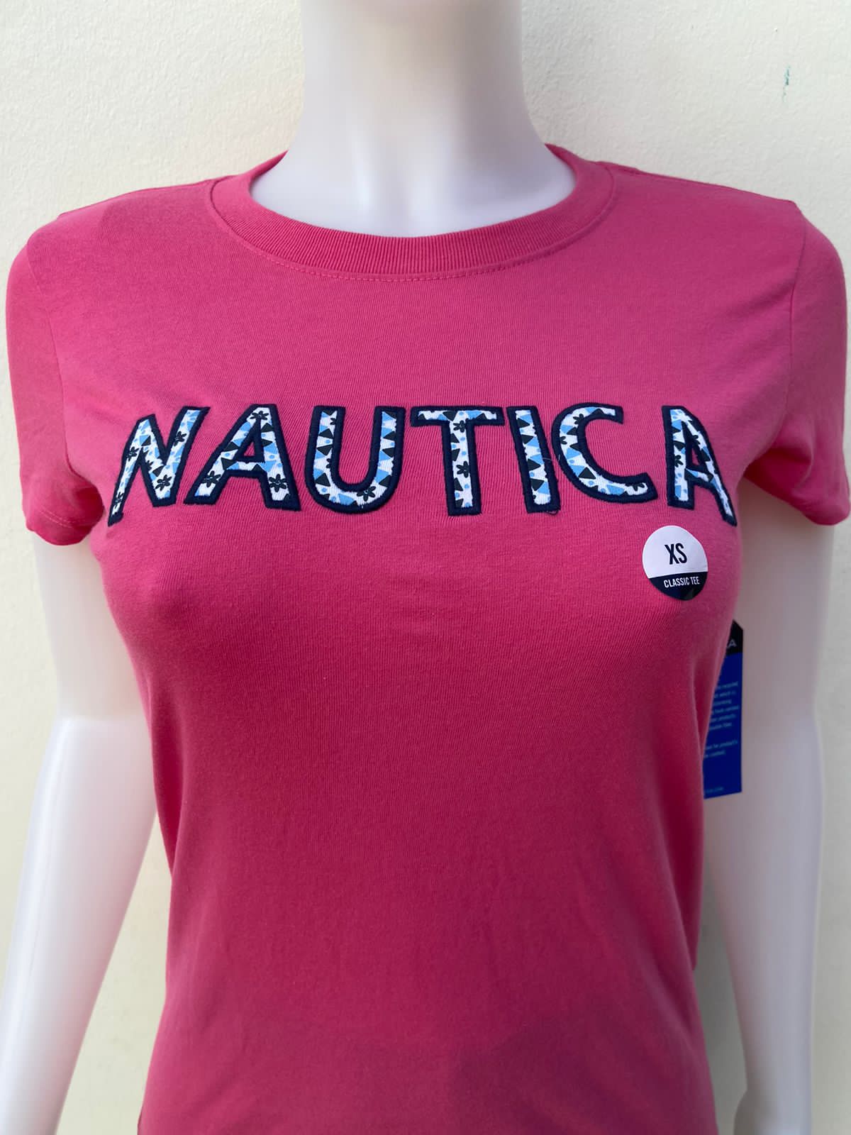 T-shirt Nautica rosado, con letras NÁUTICA en color blanco con diseño negro y azul.