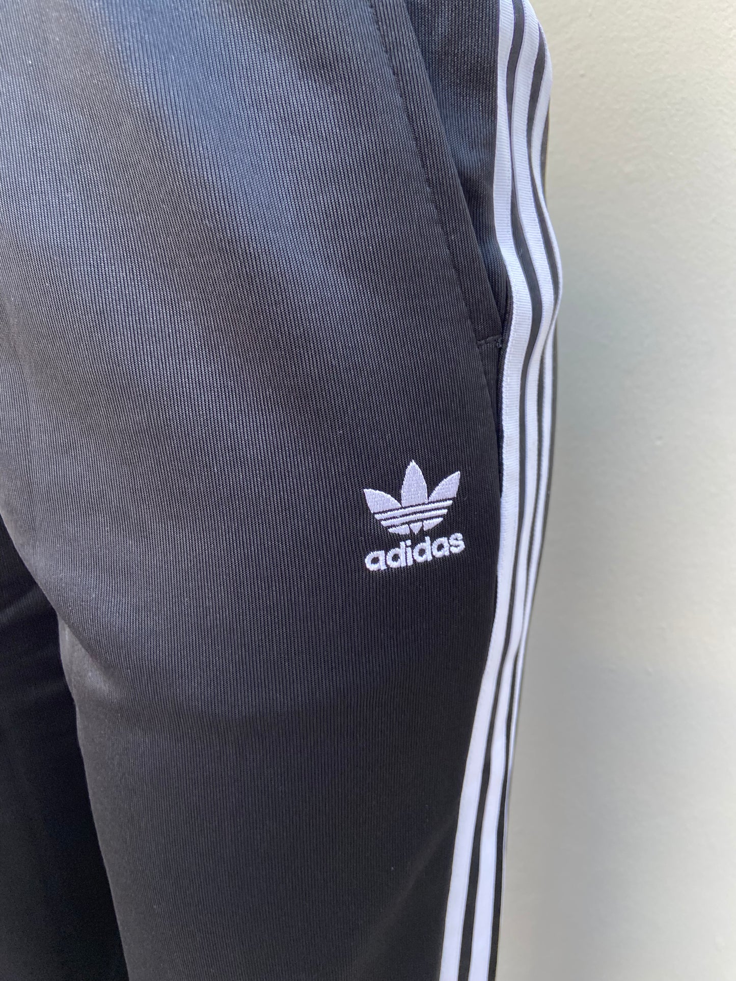 Pantalon Adidas original de color negro en tela deportiva con bolsillo a los lados diseño de letras y logo ADIDAS a un lado en color blanco con raya a los lados blanca y ruedo doblado