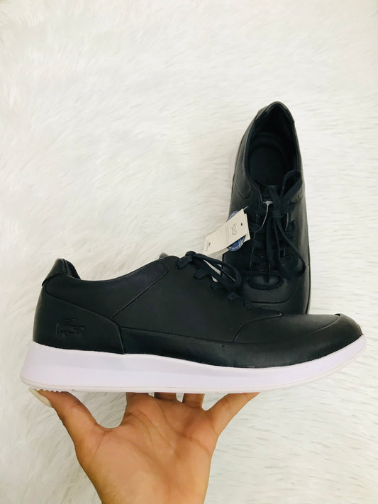 Zapato Lacoste original, color negro con parte de abajo blanca, logotipo pequeño de la marca en un lado en color negro poco visible.