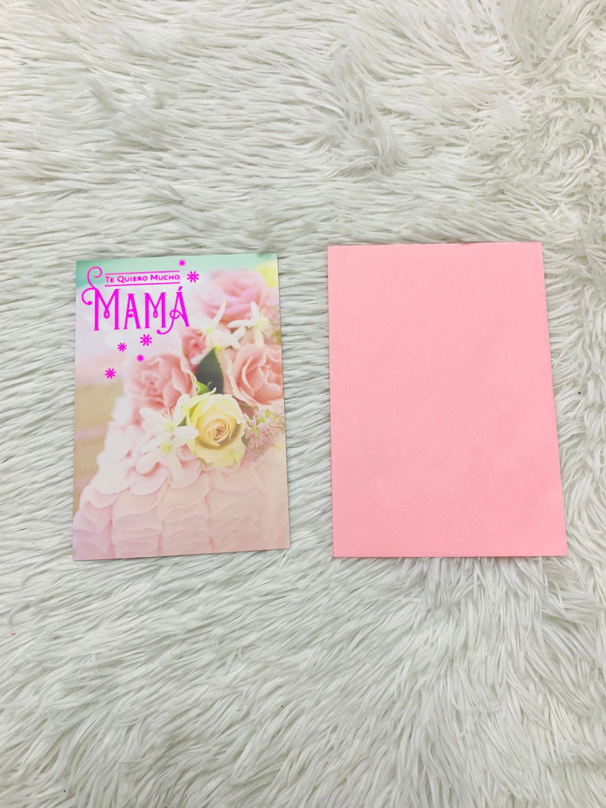 Tarjeta de felicitaciones con diseño de pliegues y flores rosadas y amarilla con diseño de letra TE QUIERO MUCHO MAMÁ en rosado oscuro