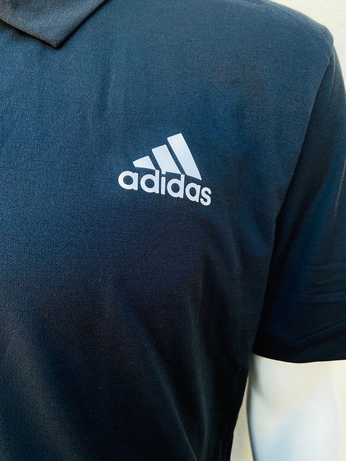 Polocher Adidas original en color negro con pequeño logo tipo de la marca y letras ADIDAS